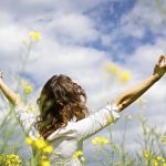 Woman standing in a field of flowers with arms stretched out enjoying the beauty of nature.