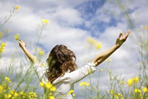 Woman standing in a field of flowers with arms stretched out enjoying the beauty of nature.